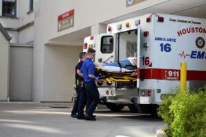 Two EMS workers loading a patient on a stretcher into the back of a Houston ambulance.