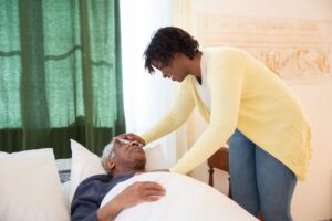 A young woman gently touching an older man's forehead as he rests in bed.