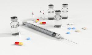 Medical supplies including a syringe, glass vials, ampoules, and various colored pills and capsules on a white background.